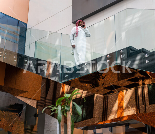 A Saudi Gulf man, making a phone call via a mobile phone inside the tourist hotel, using modern technical equipment, a working session, the concept of business management, making business deals, working remotely, e-marketing, a business trip, tourism and
