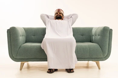 أخذ قسط من الاسترخاء و التأمل، الاستمتاع بوقت الراحة والهدوء, بورتريه لرجل عربي خليجي عماني يرتدي الدشداشة و العمامة يجلس على الاريكة يضع يديه خلف رأسه يغمض عينيه بتعابير النعاس، الشعور بالتعب والارهاق، خلفية بيضاء