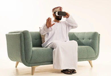 The enjoyment of watching through virtual reality glasses, technological and technical development, a portrait of an Arab Gulf Omani man wearing a dishdasha and a turban looking through 3D glasses (VR), raising his hand upwards with gestures of immersion and simulating the imaginary world, white background.