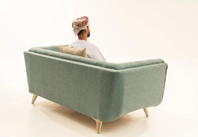 The concept of strength and masculinity, enjoying and relaxing in a calm atmosphere, a portrait from behind of an Arab Gulf Omani man wearing a dishdasha and a turban sitting on a sofa looking at something, white background.