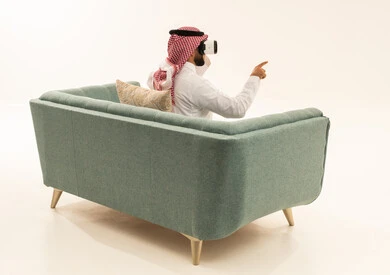 الاشارة الى مكان ما بتعابير الاندماج ومحاكاة العالم الخيالي، محاولة النقر على شيء ما, بورتريه من الخلف لرجل عربي خليجي سعودي يرتدي الثوب الابيض و الشماغ يجلس على الاريكة يضع نظارات ثلاثية الأبعاد يقوم برفع اصبع السبابة للاعلى , خلفية بيضاء