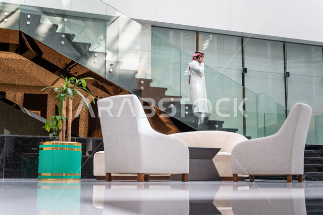 A Saudi Gulf man, making a phone call via a mobile phone inside the tourist hotel, using modern technical equipment, a working session, the concept of business management, making business deals, working remotely, e-marketing, a business trip, tourism and