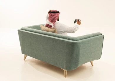 التسلية والترفيه بالفيديو جيمز في وقت الفراغ، إيماءات الخسارة وخيبة الأمل، استخدام الألعاب الإلكترونية والأجهزة الحديثة، بورتريه من الخلف لرجل عربي خليجي سعودي يرتدي الثوب الابيض و الشماغ يجلس على الاريكة يمسك عصا التحكم يضع يده على رأسه بتعابير الحسرة والحزن، خلفية بيضاء