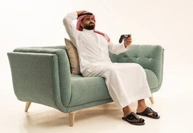 استخدام الألعاب الإلكترونية والأجهزة الحديثة، إيماءات الخسارة وخيبة الأمل، بورتريه لرجل عربي خليجي سعودي يرتدي الثوب الابيض و الشماغ يجلس على الاريكة يمسك عصا التحكم يضع يده على رأسه بتعابير الحسرة والحزن، التسلية والترفيه بالفيديو جيمز في وقت الفراغ، خلفية بيضاء
