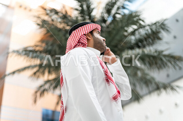 رجل خليجي سعودي ، يقوم بإجراء مكالمة هاتفية عبر الهاتف المحمول في داخل الفندق السياحي ، إستخدام أجهزة تقنية حديثة ، جلسة عمل، مفهوم إدارة الأعمال، عقد صفقات تجارية ، العمل عن بعد ، التسويق الإلكتروني، رحلة عمل ، سياحة وفندقة ، سياحة وسفر