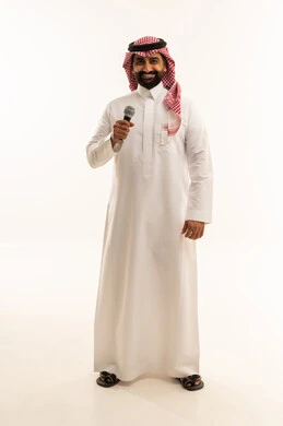 Artistic talents in the world of music, musical theater, presenting a theatrical performance, practicing the hobby of singing for fun and entertainment, a portrait of a Gulf Arab Saudi man wearing traditional attire and a ghutrah holding a microphone in his hand, full-body, white background.