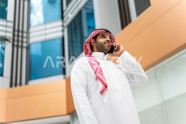 رجل خليجي سعودي ، يقوم بإجراء مكالمة هاتفية عبر الهاتف المحمول في داخل الفندق السياحي ، إستخدام أجهزة تقنية حديثة ، جلسة عمل، مفهوم إدارة الأعمال، عقد صفقات تجارية ، العمل عن بعد ، التسويق الإلكتروني، رحلة عمل ، سياحة وفندقة ، سياحة وسفر