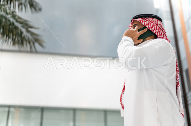 A Saudi Gulf man, making a phone call via a mobile phone inside the tourist hotel, using modern technical equipment, a working session, the concept of business management, making business deals, working remotely, e-marketing, a business trip, tourism and
