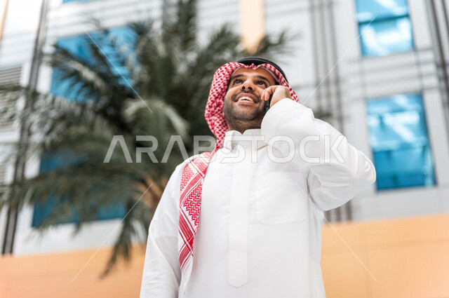 رجل خليجي سعودي ، يقوم بإجراء مكالمة هاتفية عبر الهاتف المحمول في داخل الفندق السياحي ، إستخدام أجهزة تقنية حديثة ، جلسة عمل، مفهوم إدارة الأعمال، عقد صفقات تجارية ، العمل عن بعد ، التسويق الإلكتروني، رحلة عمل ، سياحة وفندقة ، سياحة وسفر