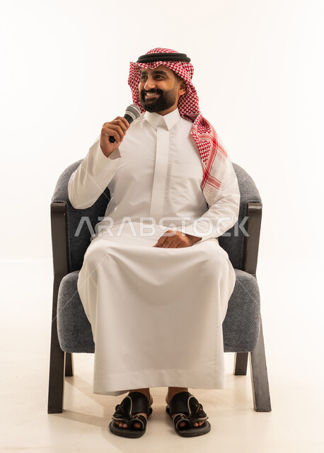 القاء الخطابات والكلمات باستخدام مكبر الصوت، القيام بالحوارات والنقاشات، بورتريه لرجل عربي خليجي عماني سعودي يرتدي الثوب الابيض و الشماغ يجلس على كرسي يحمل بيده مكبر الصوت، خلفية بيضاء