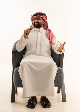 القيام بالحوارات والنقاشات،القاء الخطابات والكلمات باستخدام مكبر الصوت، بورتريه لرجل عربي خليجي عماني سعودي يرتدي الثوب الابيض و الشماغ يجلس على كرسي يحمل بيده مكبر الصوت، خلفية بيضاء