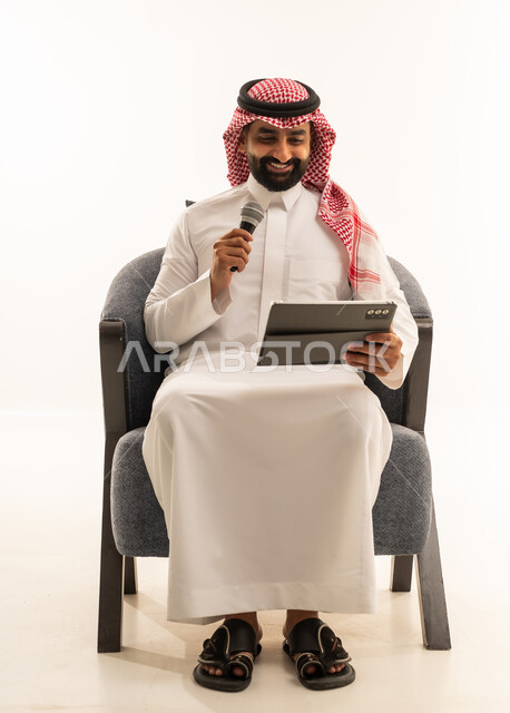 الاندماج مع الأغنية، مواهب غنائية فنية، تسجيل مقطع صوتي غنائي، بورترية لرجل عربى خليجى سعودى يرتدى الثوب التقليدى و الشماغ يجلس على الكرسى يقوم بالغناء باستخدام الميكروفون يمسك بيدية التابلت بتعابير الحماس، خلفية بيضاء