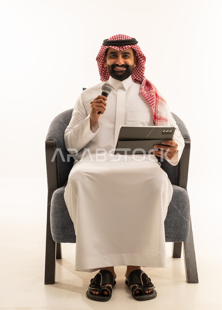 مواهب غنائية فنية، تسجيل مقطع صوتي غنائي، الاندماج مع الأغنية، بورترية لرجل عربى خليجى سعودى يرتدى الثوب التقليدى و الشماغ يجلس على الكرسى يقوم بالغناء باستخدام الميكروفون يمسك بيدية التابلت بتعابير الحماس، خلفية بيضاء