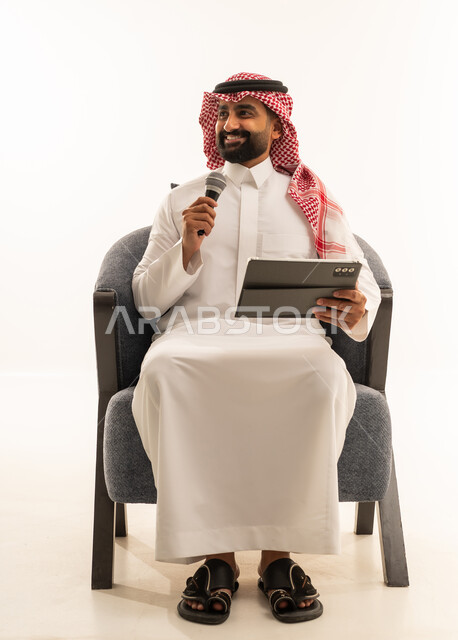 تسجيل مقطع صوتي غنائي، مواهب غنائية فنية، الاندماج مع الأغنية، بورترية لرجل عربى خليجى سعودى يرتدى الثوب التقليدى و الشماغ يجلس على الكرسى يقوم بالغناء باستخدام الميكروفون يمسك بيدية التابلت بتعابير الحماس، خلفية بيضاء