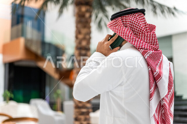 A Saudi Gulf man, making a phone call via a mobile phone inside the tourist hotel, using modern technical equipment, a working session, the concept of business management, making business deals, working remotely, e-marketing, a business trip, tourism and