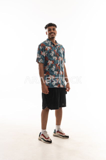 Standing sideways and looking at the camera with a smile, an Arab Gulf Omani man wearing casual attire, gestures of happiness, portrait with a white background, full body.