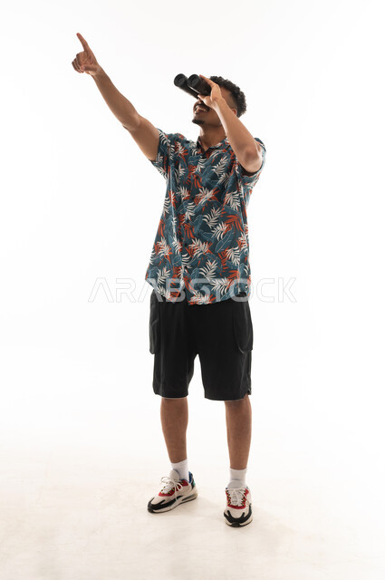 الاشارة للاعلى باصبع السبابة , رجل عربي عماني خليجي يرتدي الزي الكاجوال يحمل المنظار المقرب لرؤية الاشياء البعيدة , بورتريه خلفية بيضاء , الجسم بالطول الكامل