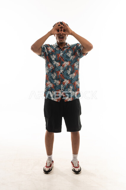 حركة دائرية باصبعي السبابة و الابهام اشارة للمنظار المقرب للاشياء البعيدة , رجل عربي خليجي عماني يرتدي الزي الكاجوال ينظر للكاميرا , ايماءات السعادة , الجسم بالطول الكامل , بورتريه خلفية بيضاء