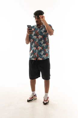 Lifting the sunglasses off the eyes for clearer vision, an Arab Gulf Omani man wearing casual attire holding a mobile phone, portrait with a white background, full body.