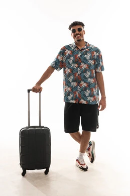 الاستناد على حقيبة السفر الصغيرة , رجل عربي خليجي عماني يرتدي الزي الكاجوال و النظارة الشمسية يقف بسعادة امام الكاميرا , الجسم بالطول الكامل , بورتريه خلفية بيضاء