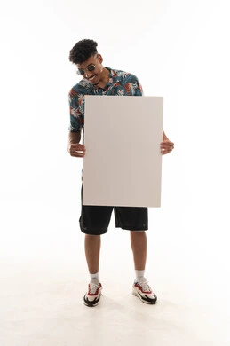 Looking happily at the large paper, an Arab Gulf Omani man wearing casual attire holds a blank sheet in front of the camera, portrait with a white background, full body.
