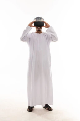 A Gulf Arab Omani man wearing a white dishdasha and a turban is holding virtual reality glasses in his hands, with gestures of excitement and thrill, full-body shot, white background portrait.
