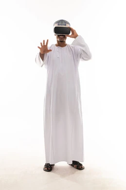 نظارة محاكاة الواقع الحقيقي , رجل عربي خليجي عماني يرتدي الدشداشة البيضاء و العمامة يلبس نظارة الواقع الافتراضي , الشعور بالاثارة و التشويق , الجسم بالطول الكامل , بورتريه خلفية بيضاء
