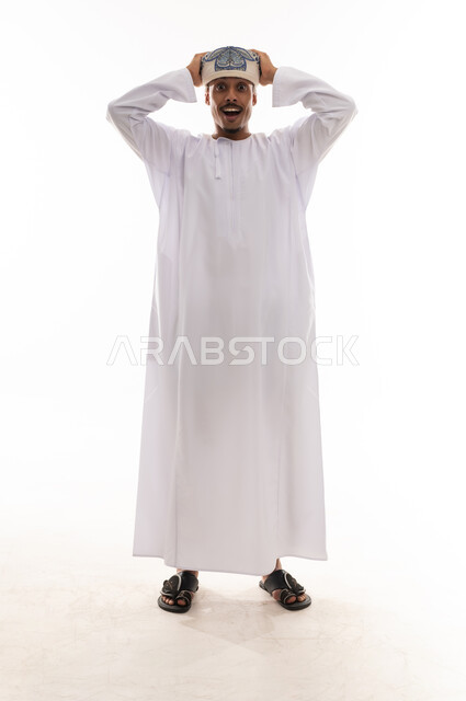 تعابير الذهول و الاندهاش , رجل عربي خليجي عماني يرتدي الدشداشة البيضاء و العمامة يضع يده فوق راسه اشارة الي الشعور بالدهشة , النظر للكاميرا , بورتريه خلفية بيضاء , الجسم بالطول الكامل