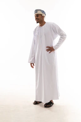 رجل عربي خليجي عماني يرتدي الدشداشة البيضاء و العمامة يضع يده في وسط الجسد , النظر للجانب ,ايماءات الابتسامة , بورتريه خلفية بيضاء , الجسم بالطول الكامل