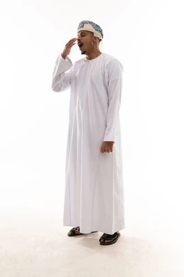 التثاؤب و الشعور بالنعاس , رجل عربي خليجي عماني يرتدي الدشداشة البيضاء و العمامة يضع كف اليد امام الفم و يتثاءب , الجسم بالطول الكامل , بورتريه خلفية بيضاء