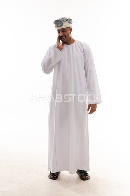 تعابير الشعور بالالم والانزعاج من الاسنان , رجل عربي خليجي عماني يرتدي الدشداشة البيضاء و العمامة يشعر بوجع الاسنان الشديد ,وضع اصابع اليد على الخد , بورتريه خلفية بيضاء , الجسم بالطول الكامل