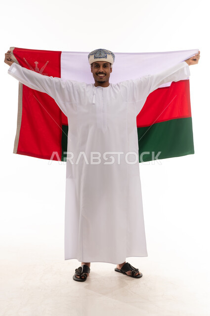 The Omani flag is raised in happiness, a Gulf Arab Omani man wearing a white dishdasha and turban, feeling pride and belonging, full-length body, portrait with a white background.