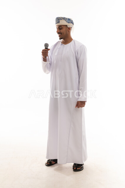 Looking at the microphone while singing, an Arab Gulf Omani man wearing a white dishdasha and a turban enjoying his time singing songs, expressions of happiness and joy, portrait with a white background, full body.