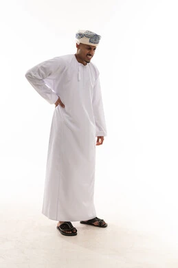 رجل عربي خليجي عماني يرتدي دشداشة بيضاء و العمامة يمسك العمود الفقري اشارة الي الالم الشديد , الشعور بالمرض و الاعياء , بورتريه خلفية بيضاء , الجسم بالطول الكامل