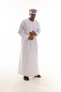 تعابير الشعور بالالم و التعب , رجل عربي خليجي عماني يرتدي الدشداشة البيضاء و العمامة يضع يديه على بطنه اشارة يشعر بالالم الشديد , الجسم بالطول الكامل , بورتريه خلفية بيضاء