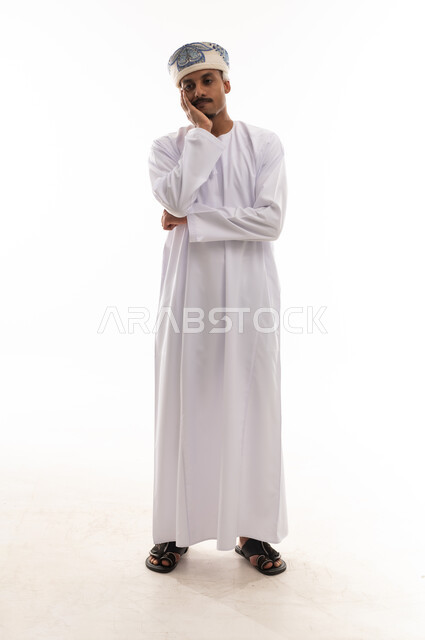 وضع كف اليد على الوجنة اشارة الي الاحباط و الحزن , رجل عربي خليجي عماني يرتدي الدشداشة البيضاء و العمامة , ايماءات الانزعاج و الضيق , الوقوف امام الكاميرا , الجسم بالطول الكامل, بورتريه خلفية بيضاء