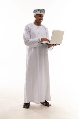 A man easily carries a small laptop, an Arab Gulf Omani man wearing a white dishdasha and turban is typing on the keyboard, showing gestures of happiness and excitement, portrait with a white background, full body.