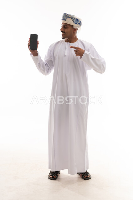 A finger pointing on a mobile phone, an Arab Gulf Omani man wearing a white dishdasha and a turban, displaying a blank black screen, gestures of happiness and smiling, white background, full-body portrait.