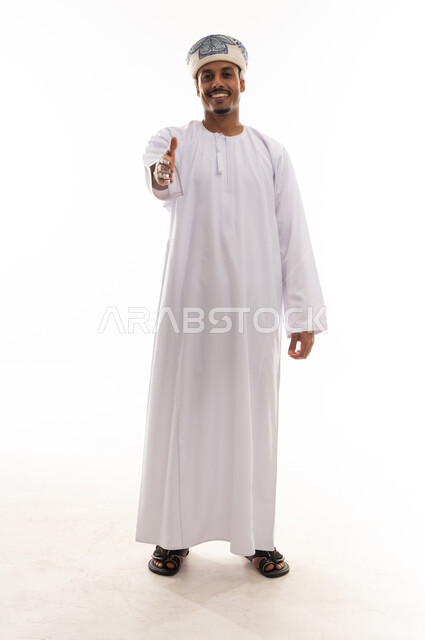 فرد الذراع بالكامل و مد اليد للسلام , رجل عربي خليجي عماني يرتدي الدشداشة البيضاء و العمامة , الوقوف امام الكاميرا , ايماءات الابتسامة و السعادة , الجسم بالطول الكامل , بورتريه خلفية بيضاء