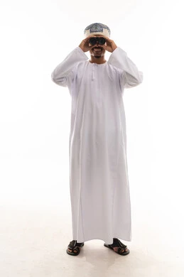 النظر و الابتسامة امام الكاميرا , رجل عربي خليجي عماني يرتدي الدشداشة البيضاء و العمامة يحمل المنظار المقرب و ينظر الى شئ ما , ايماءات السعادة و البهجة , الجسم بالطول الكامل , بورتريه خلفية بيضاء