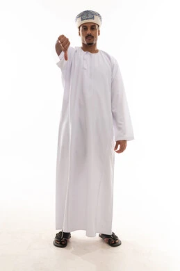 رجل عربي خليجي عماني يرتدي الدشداشة البيضاء و العمامة يرفع اصبع الابهام لاسفل علامة على عدم الاعجاب , ايماءات الانزعاج من شئ ما , بورتريه خلفية بيضاء , الجسم بالطول الكامل