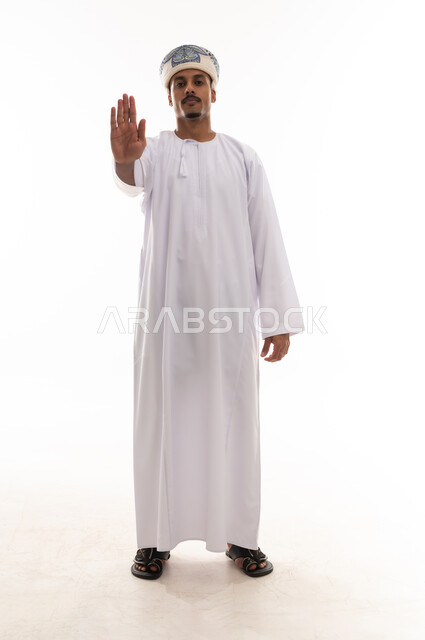 وضع كف اليد امام الكاميرا علامة على التوقف و طلب الوقوف , رجل عربي خليجي عماني يرتدي دشداشة بيضاء و عمامة , بورتريه خلفية بيضاء , الجسم بالطول الكامل , علامة ممنوع الاقتراب اكثر  , تعابير الاستياء و الضيق