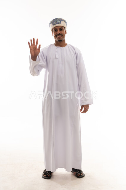 رفع باطن الكف امام الكاميرا اشارة التحية و السلام , رجل عربي خليجي عماني يرتدي الدشداشة البيضاء و العمامة , ايماءات السعادة و الفرحة اثناء اللقاء , بورتريه خلفية بيضاء , الجسم بالطول الكامل , اشارة رقم خمسة