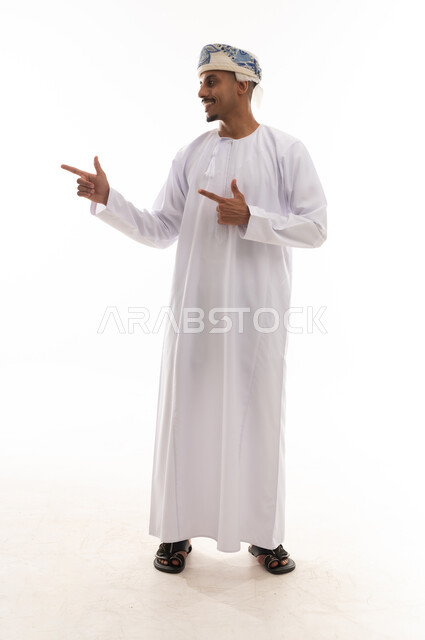 رفع اصبعي السبابة للجانب اشارة الي شئ ما , رجل عربي خليجي عماني يرتدي الدشداشة البيضاء و العمامة , النظر الي الجانب , الجسم بالطول الكامل , خلفية بيضاء