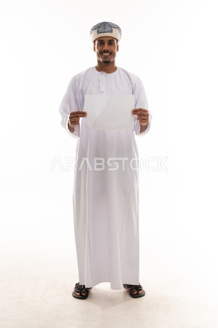 رجل عربي خليجي عماني يرتدي دشداشة بيضاء و عمامة يحمل ورقة صغيرة , نظرة امامية للكاميرا , ايماءات السعادة , الجسم بالطول الكامل , بورتريه خلفية بيضاء