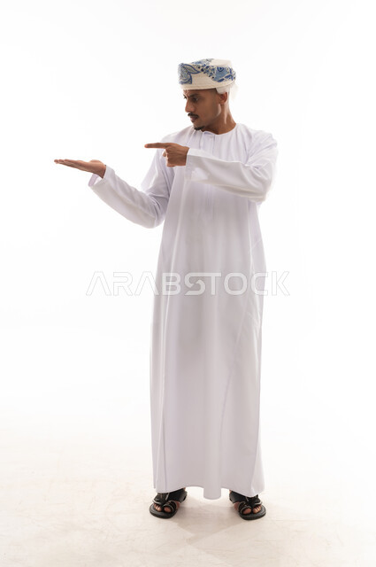 الاشارة باصبع السبابة للجانب بنظرة جدية , رجل عربي خليجي عماني يرتدي دشداشة بيضاء و عمامة يقف امام الكاميرا , الجسم بالطول الكامل , بورتريه خلفية بيضاء