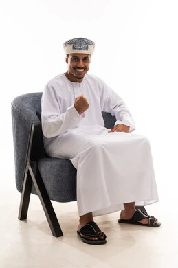 تعابير الفرحة عند تحقيق الفوز , رجل عربي خليجي عماني يرتدي دشداشة بيضاء و عمامة يقفل قبضة يد واحدة و يرفعها للاعلى اشارة الى السعادة و البهجة , بورتريه خلفية بيضاء , الجسم بالطول الكامل , نظرة أمامية للكاميرا