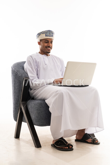 كتابة التقارير و ارسال البريد الالكتروني للاغراض المهنية و الشخصية بطريقة سهلة باستخدام احدث الاجهزة التقنية , رجل عربي خليجي عماني يرتدي دشداشة بيضاء و العمامة يحمل الحاسوب المتنقل , بورتريه خلفية بيضاء , الجسم بالطول الكامل