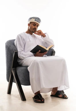 Portrait with a white background, full-length body, an Arab Omani Gulf man wearing a white dishdasha and a turban, placing his hand on his face as a sign of focus and immersion in enjoyable reading.