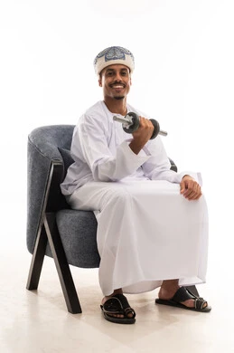 استعراض القوة البدنية امام الكاميرا , رجل عربي خليجي عماني يرتدي العمامة ودشداشة بيضاء يرفع الوزن الثقيل بثبات , خلفية بيضاء , الجسم بالطول الكامل , نظرة أمامية